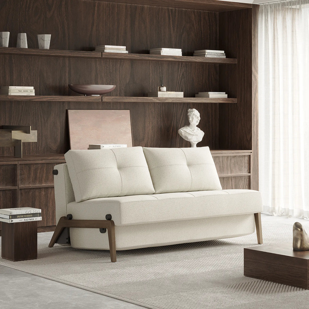 natural tweed fabric 2 seater loveseat sofa bed. Armless with dark wood legs. In living room with wood walls and shelving
