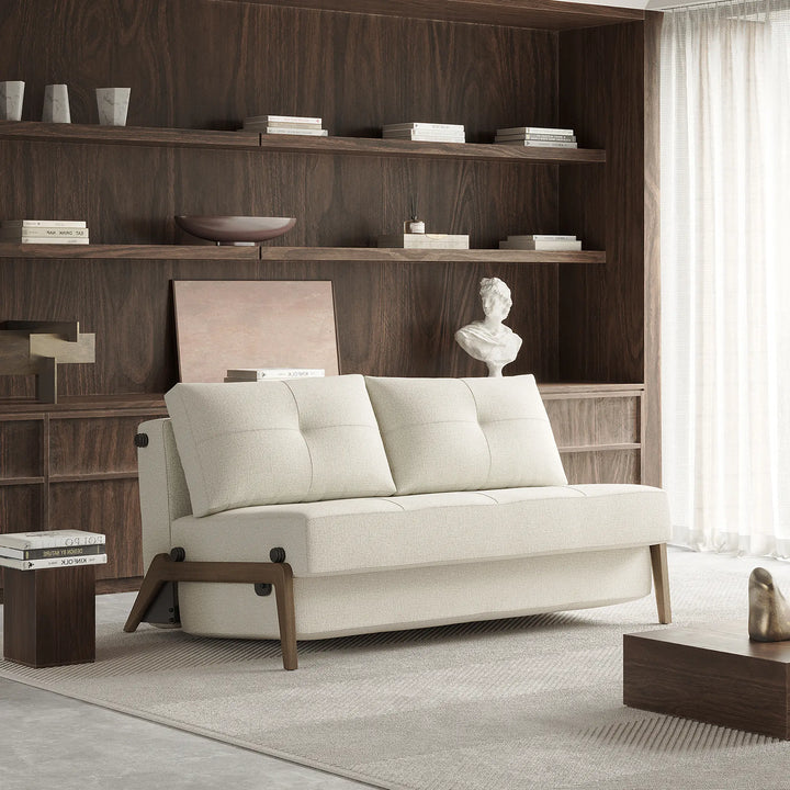natural tweed fabric 2 seater loveseat sofa bed. Armless with dark wood legs. In living room with wood walls and shelving